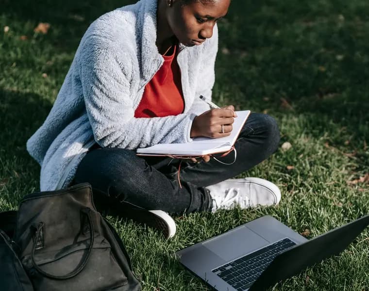 A student studying with her laptop and notebook outdoors